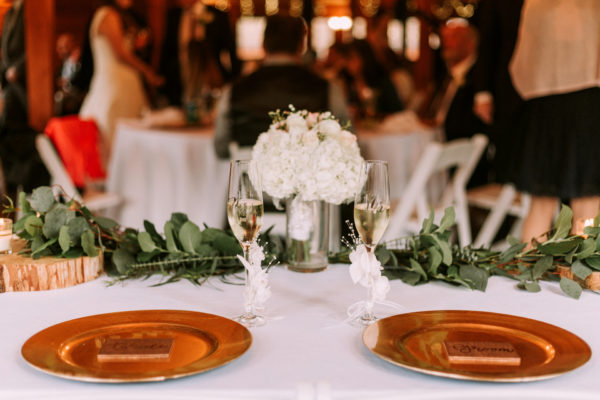 Gold chargers on white cloth with elegant white hydrangeas in a vase surrounded by eucalyptus, It's all in the Details